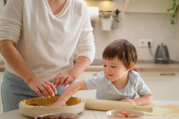 Toddler helping mom roll out pie dough 